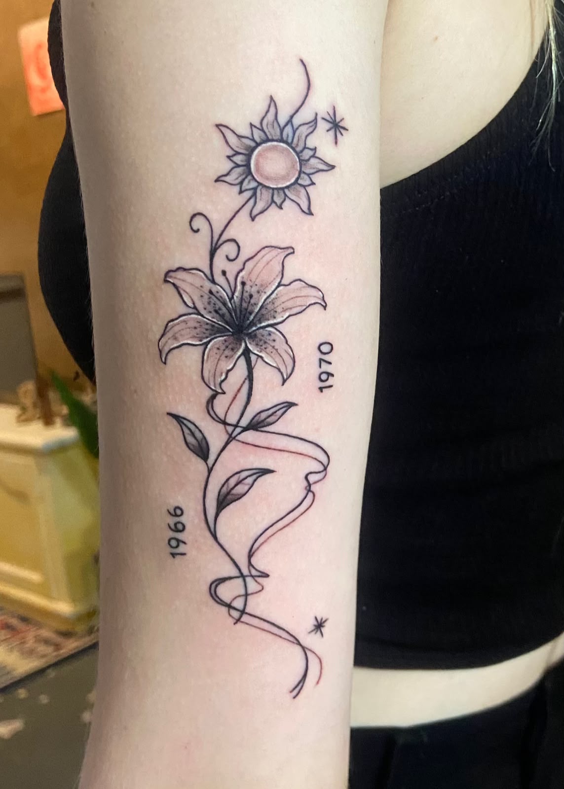 Tatuagem delicada de flores, rosto em linha e datas no braço